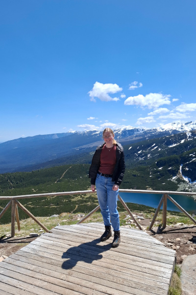 Lorena auf einer Aussichtsplattform, im Hintergrund Berge, Wald und ein See
