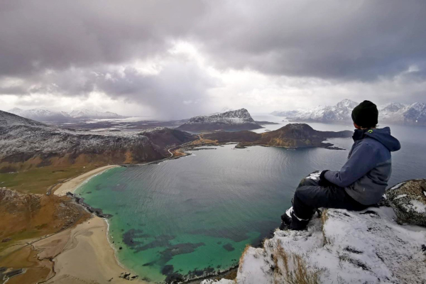 Wolfgang sitzt auf einem verschneiten Felsvorsprung und blickt auf Berge, die aus dem Meer ragen
